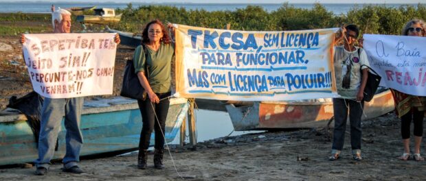 Activist Eliane Roxo holds a banner denouncing TKCSA's pollution of the bay