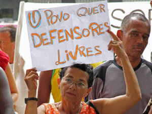 A woman holds a sign that says "The people want free defenders"