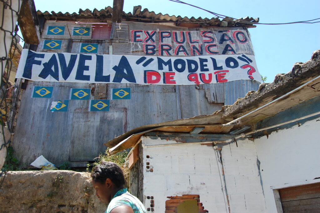 The phrases “Favela 'model' of  what?” and “White eviction” (local term for 'gentrification') on a house in Santa Marta demonstrate the dissatisfaction of the residents. Photo by Miriane Peregrino