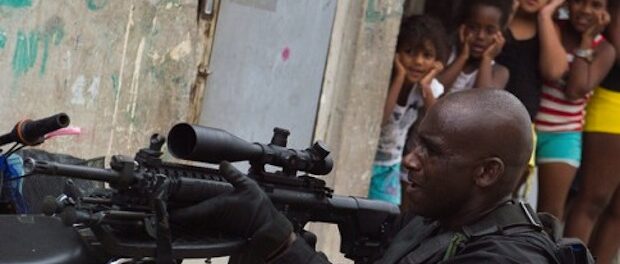 A police officer sets up his rifle under the gaze of children. Photo by O Nacional