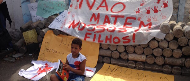 Boy with book sits in front of protest sign that reads "Don't kill our sons!"