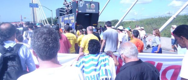 Maria da Penha wears the well-known Vila Autódromo flag as the protest crosses an iconic bridge in Barra da Tijuca. Photo from Nidivaldo Marcário Oliveria Facebook page.
