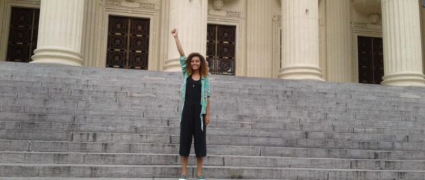 Thaisa Santos in front of ALERJ with her fist raised. Photo by: Thaisa Santos.